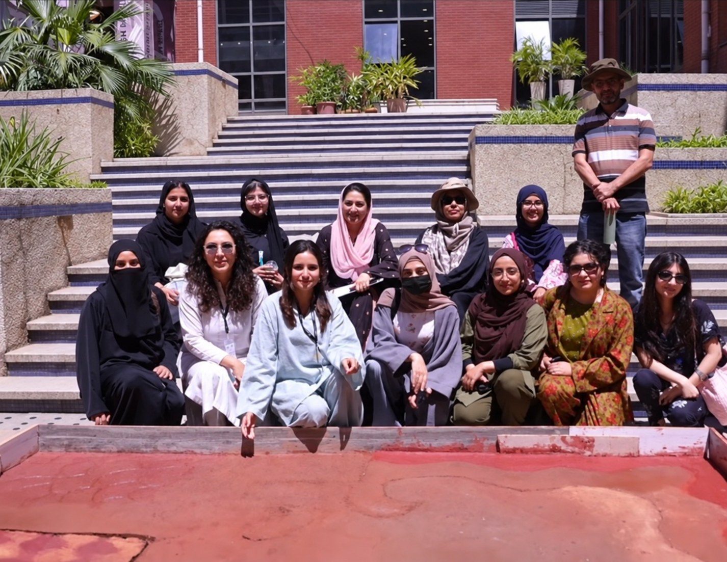 Workshop participants in Pakistan seated on campus steps behind the red earthen floor they made together