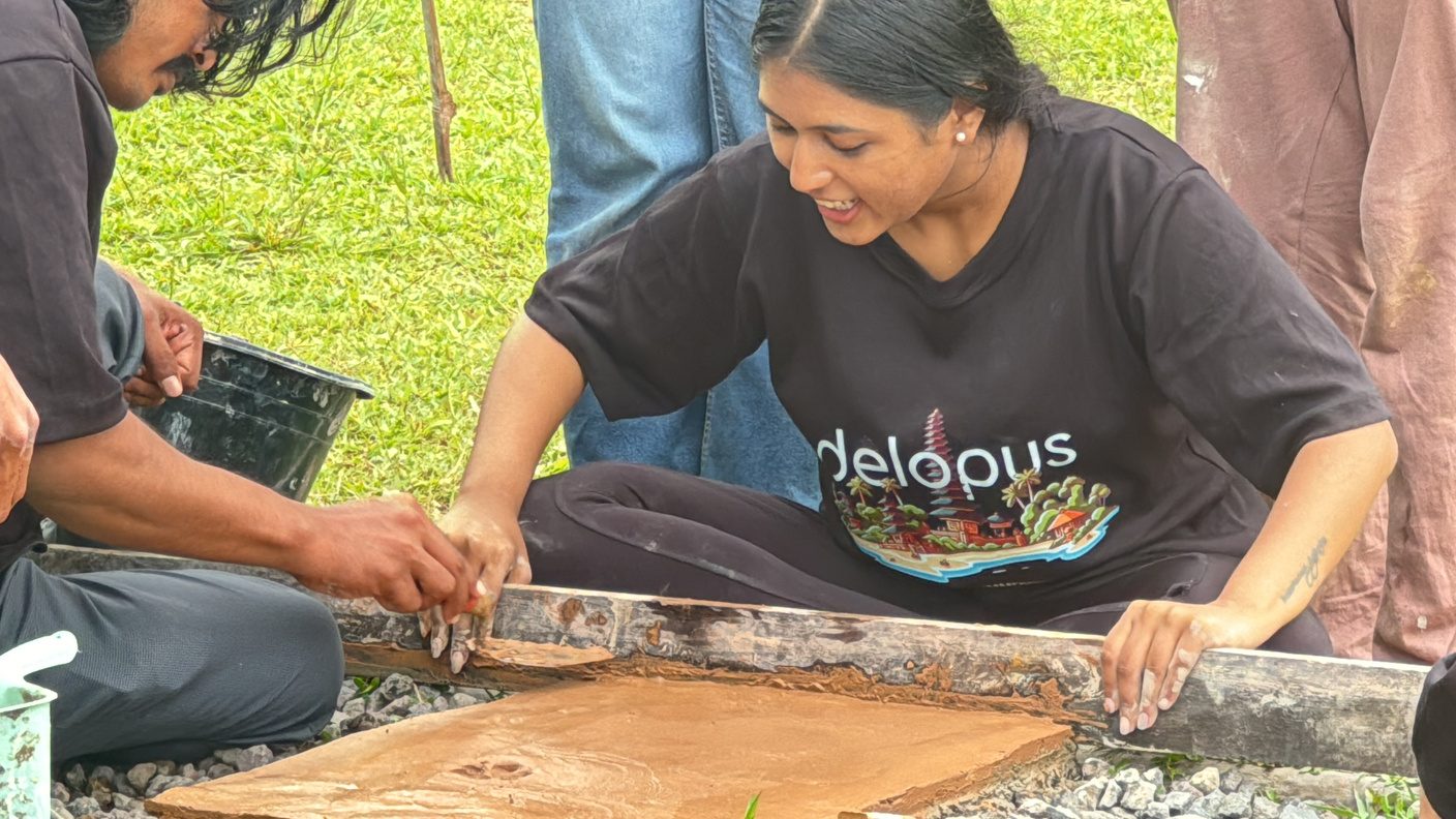 A participant levelling an earthen floor by hand with a straight edge during a workshop in Bali
